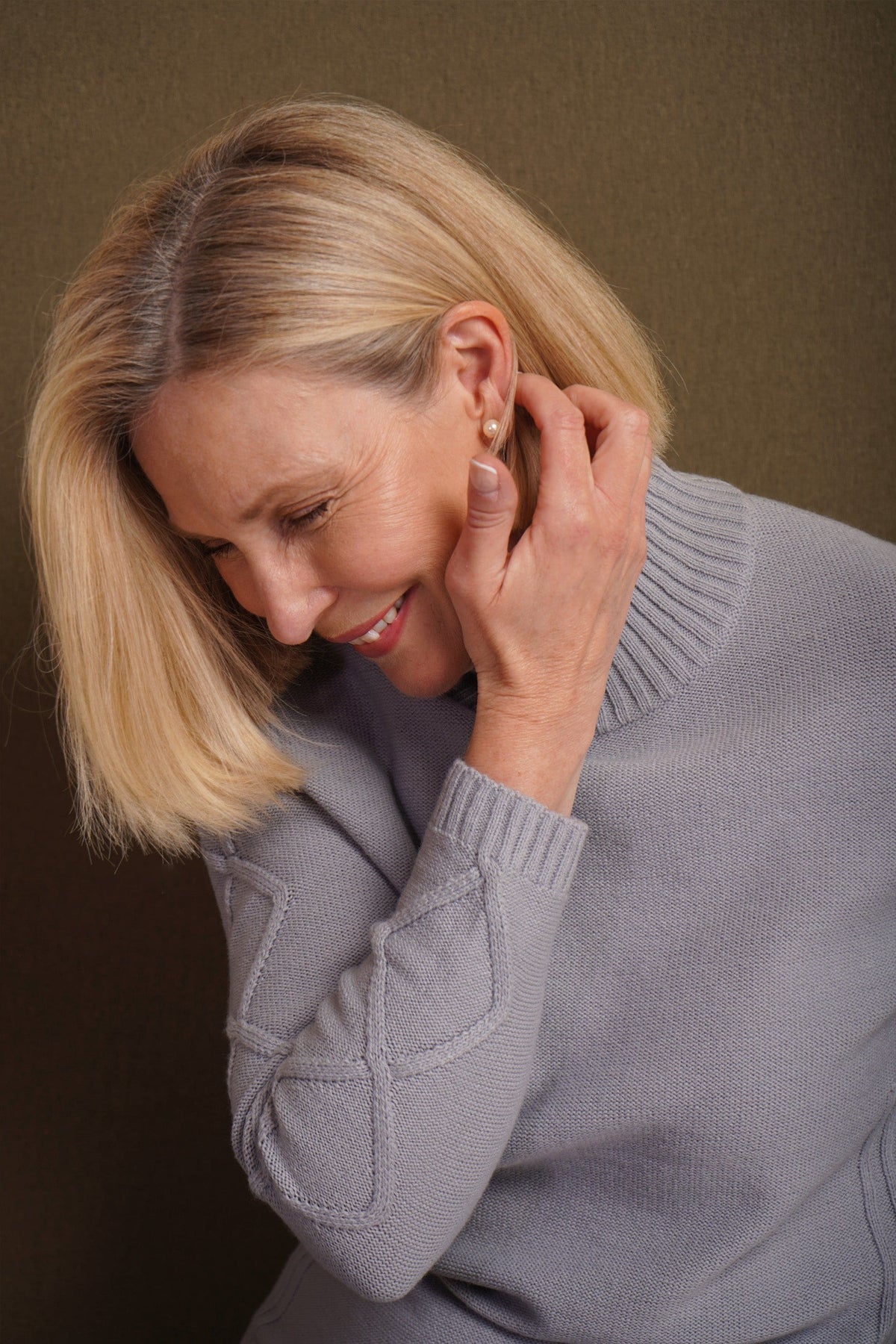 Woman sitting and smiling, wearing a relaxed cable knit turtleneck jumper with ribbed cuffs and diamond patterned sleeves, paired with corduroy trousers._11