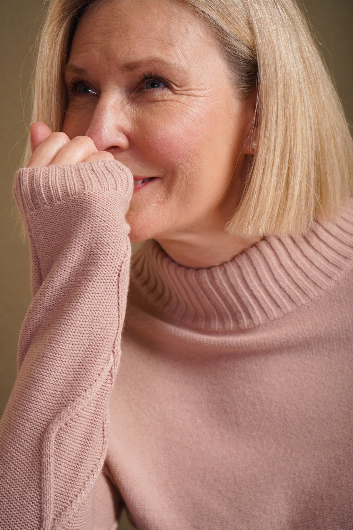 Woman sitting and smiling, wearing a relaxed cable knit turtleneck jumper with ribbed cuffs and diamond patterned sleeves, paired with corduroy trousers._14