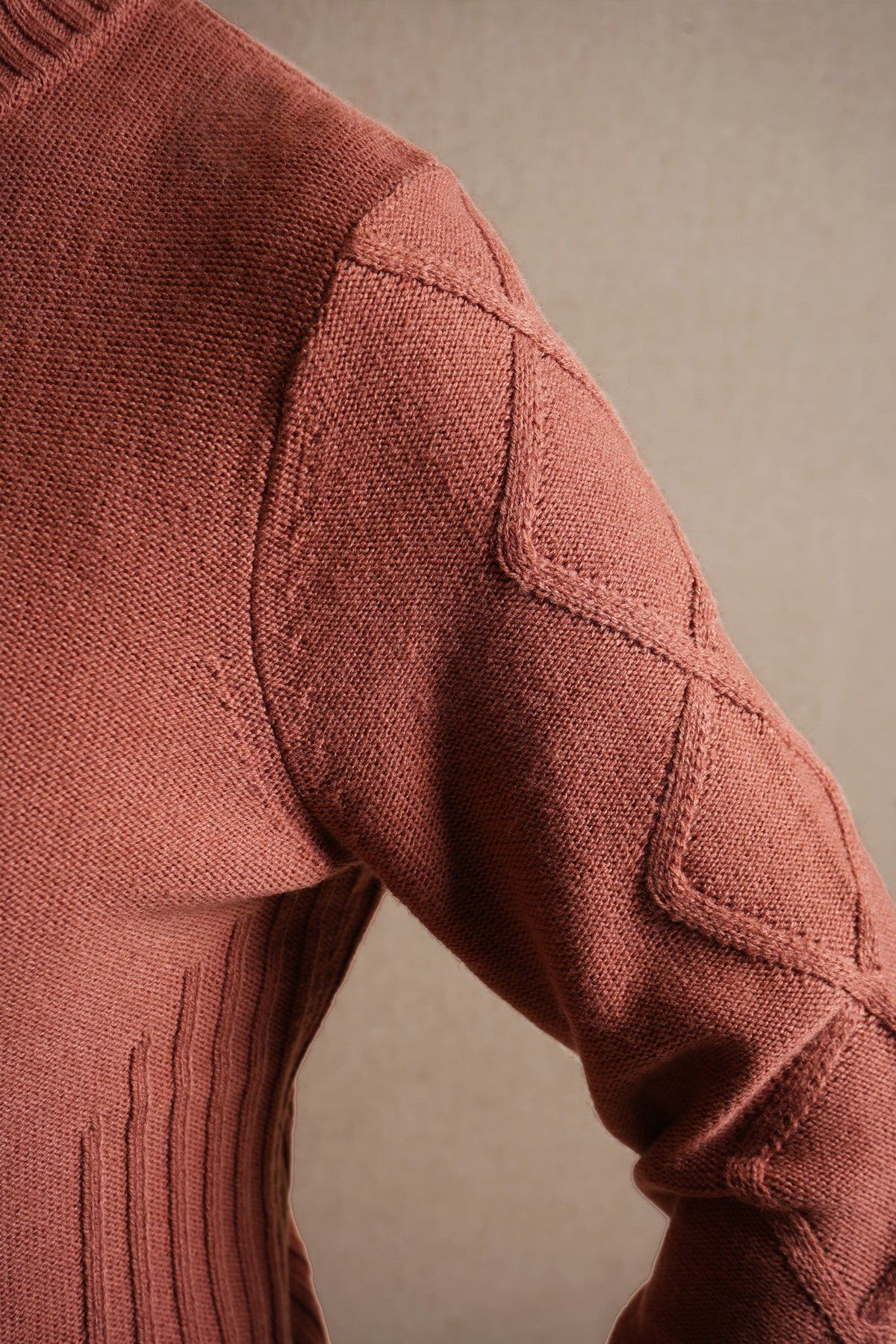 Woman sitting and smiling, wearing a relaxed cable knit turtleneck jumper with ribbed cuffs and diamond patterned sleeves, paired with corduroy trousers._5