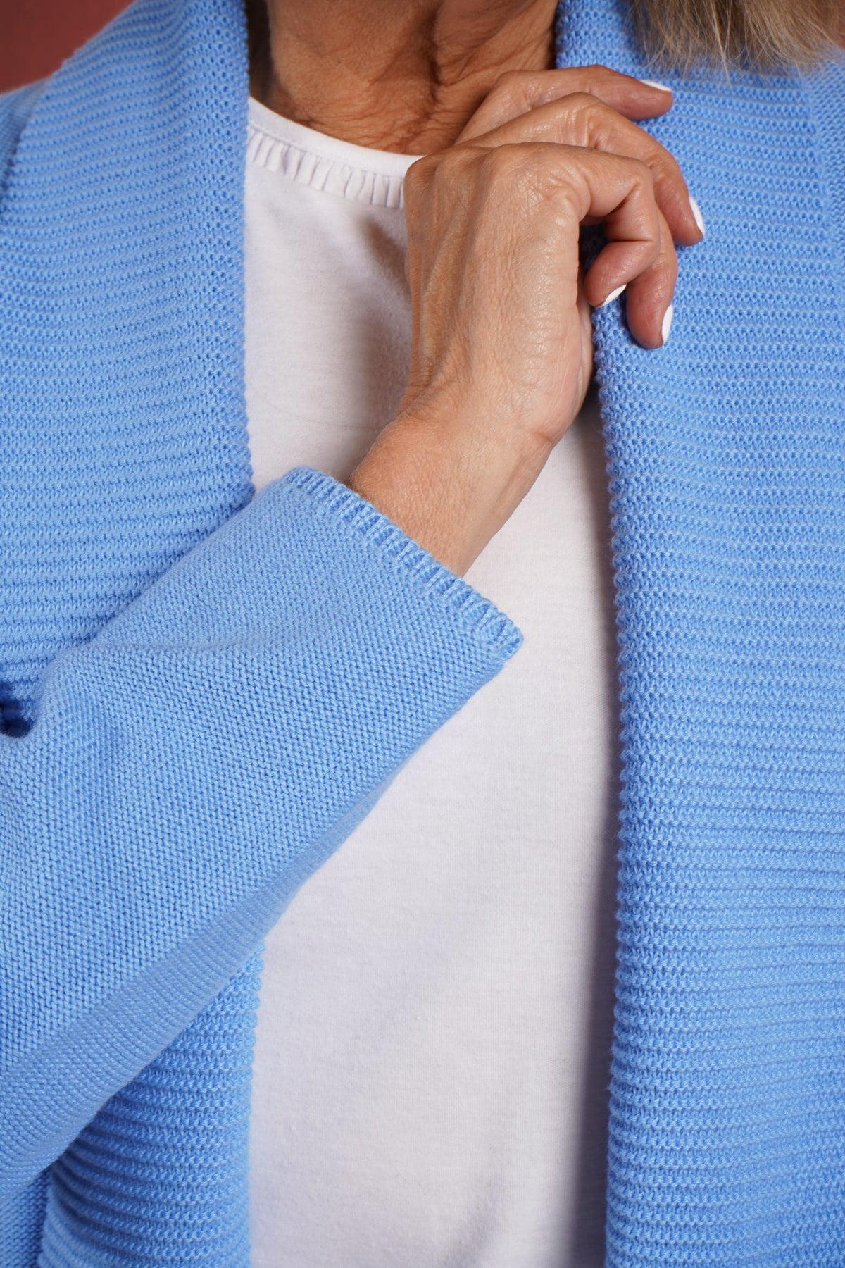 Woman wearing a longline open front knitted cardigan with a wide ribbed shawl collar and front patch pockets over a plain top and jeans._5