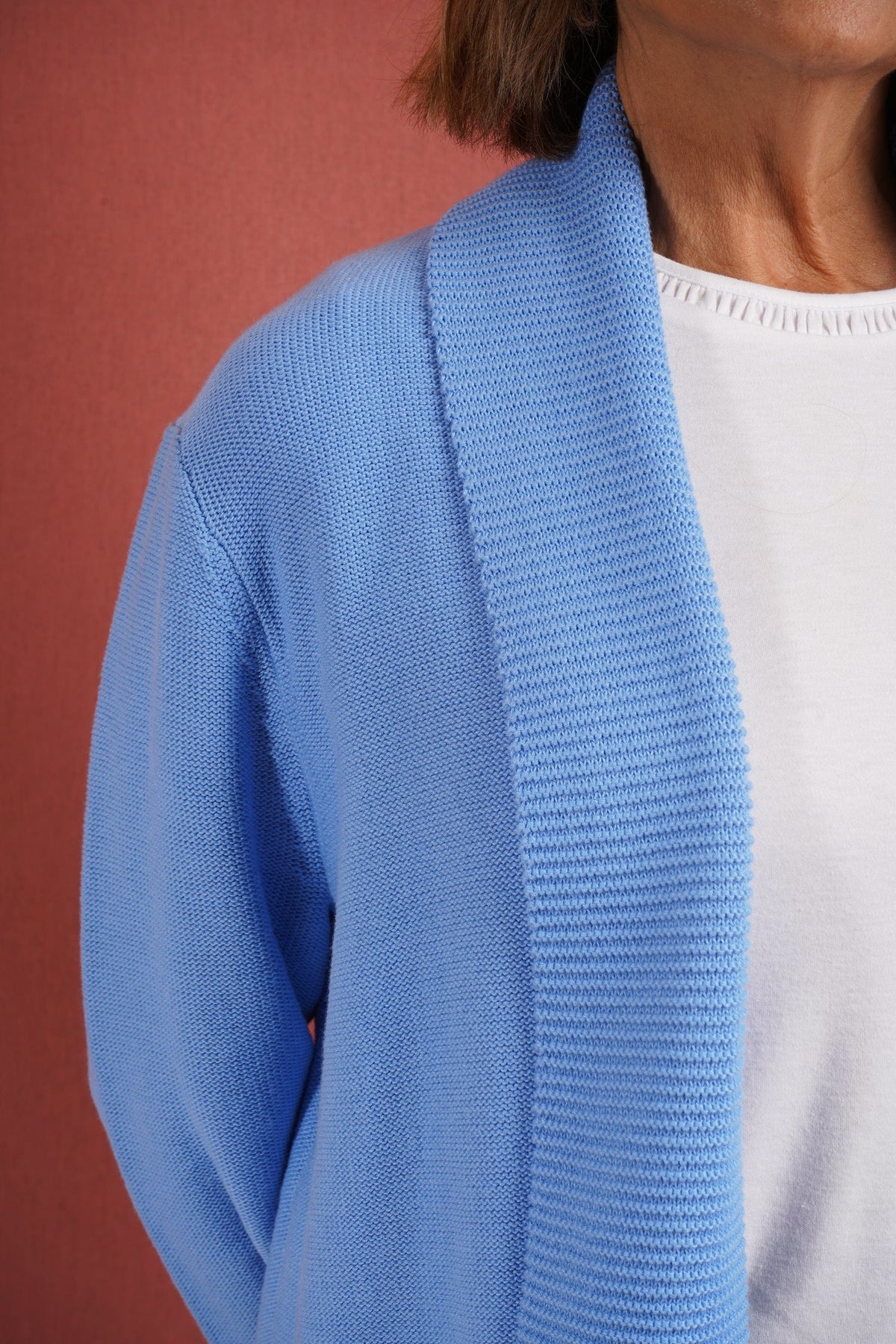 Woman wearing a longline open front knitted cardigan with a wide ribbed shawl collar and front patch pockets over a plain top and jeans._6