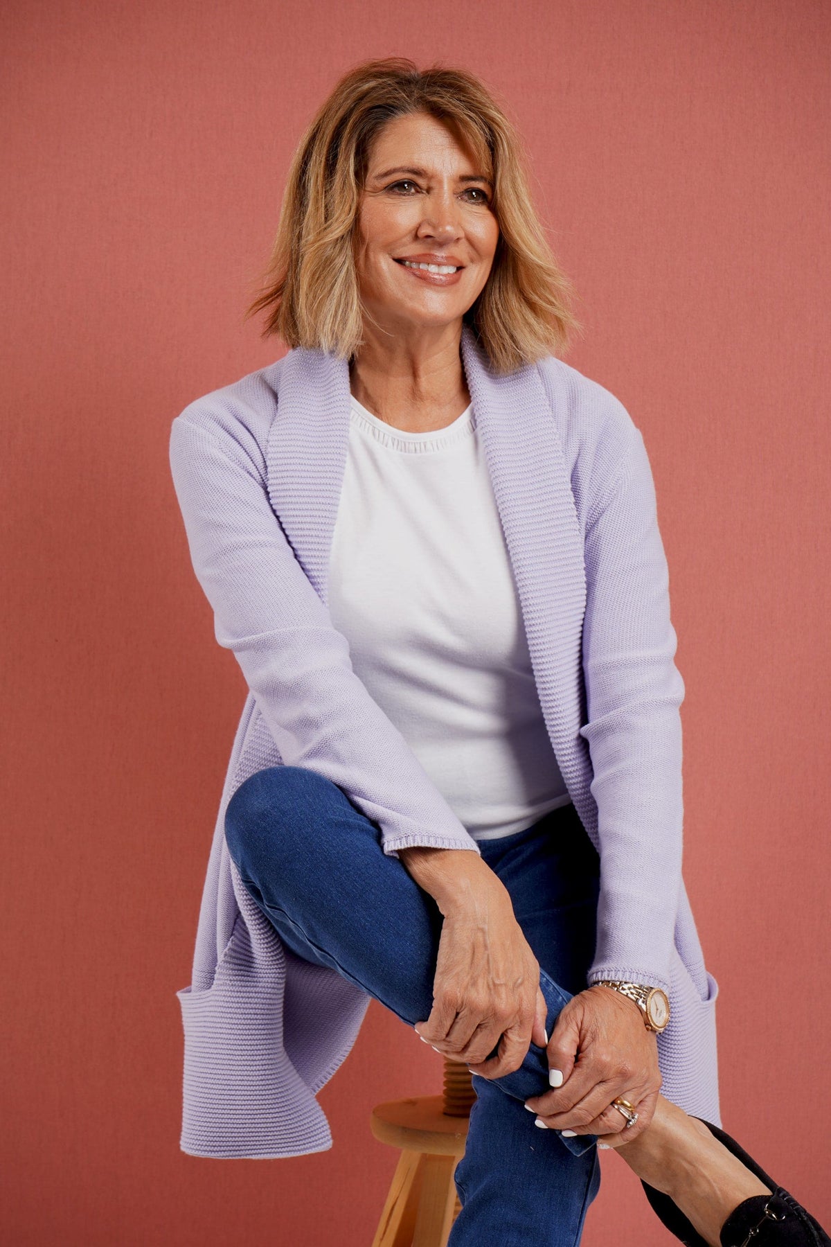 Woman wearing a longline open front knitted cardigan with a wide ribbed shawl collar and front patch pockets over a plain top and jeans._7