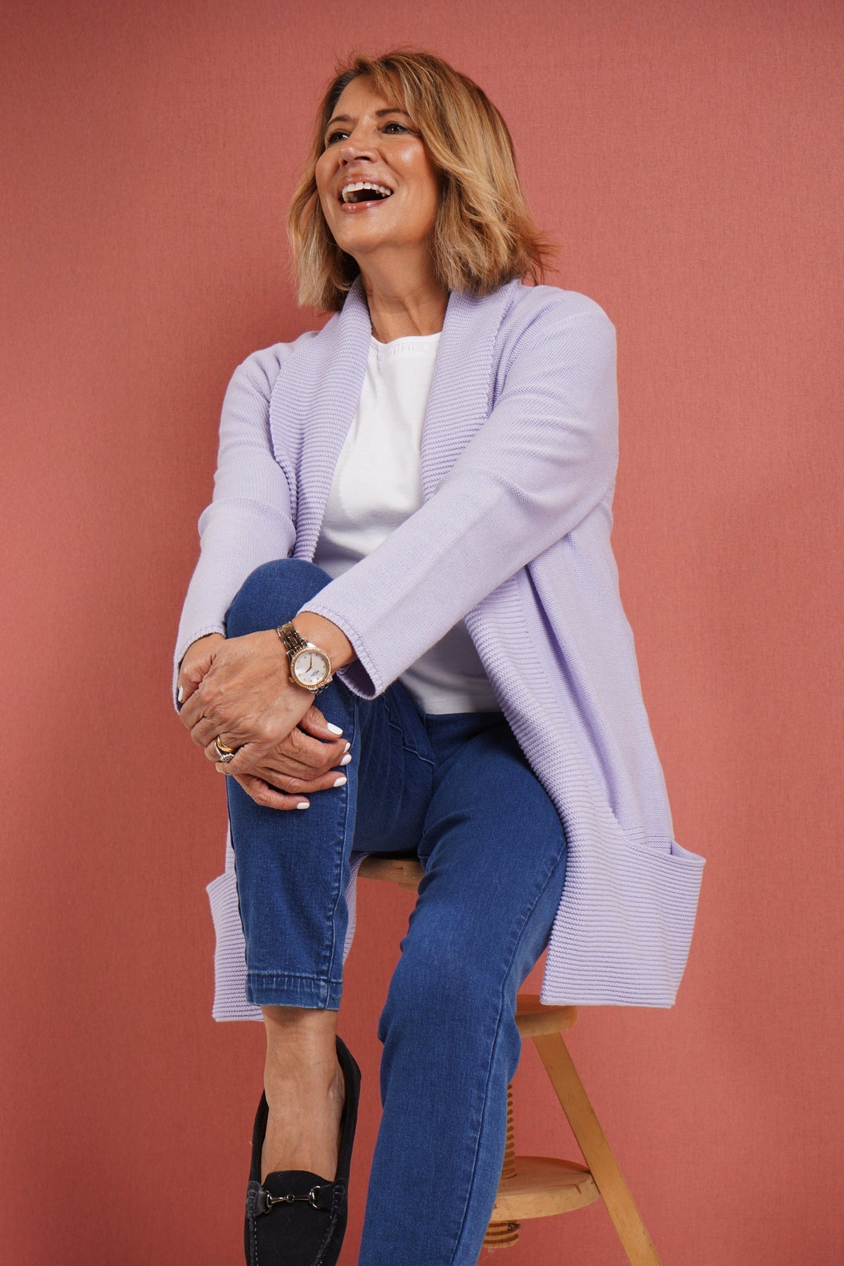Woman wearing a longline open front knitted cardigan with a wide ribbed shawl collar and front patch pockets over a plain top and jeans._8