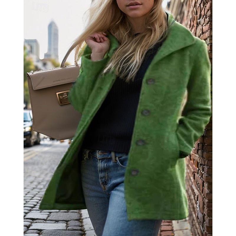 Green women's short coat with a notched collar, dark buttons, and side pockets, photographed beside a brick wall.
