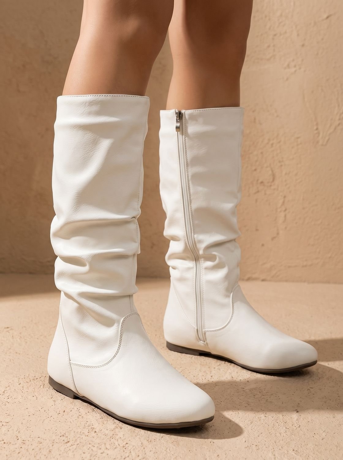 Pair of white slouchy knee-high boots with softly gathered shafts, round toes, side zippers, and low flat heels.