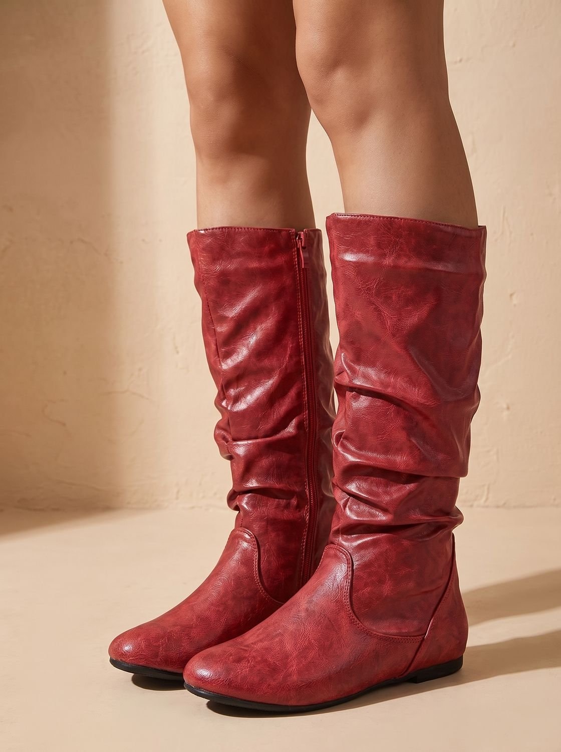 Red knee-high flat boots standing together, shown front-on with prominent ruched shafts and rounded toes.