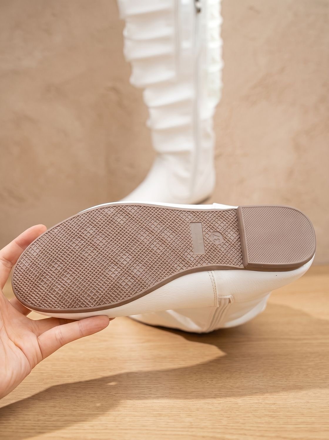 White boot sole held above a wood surface, showing the textured tread and low flat heel from underneath.