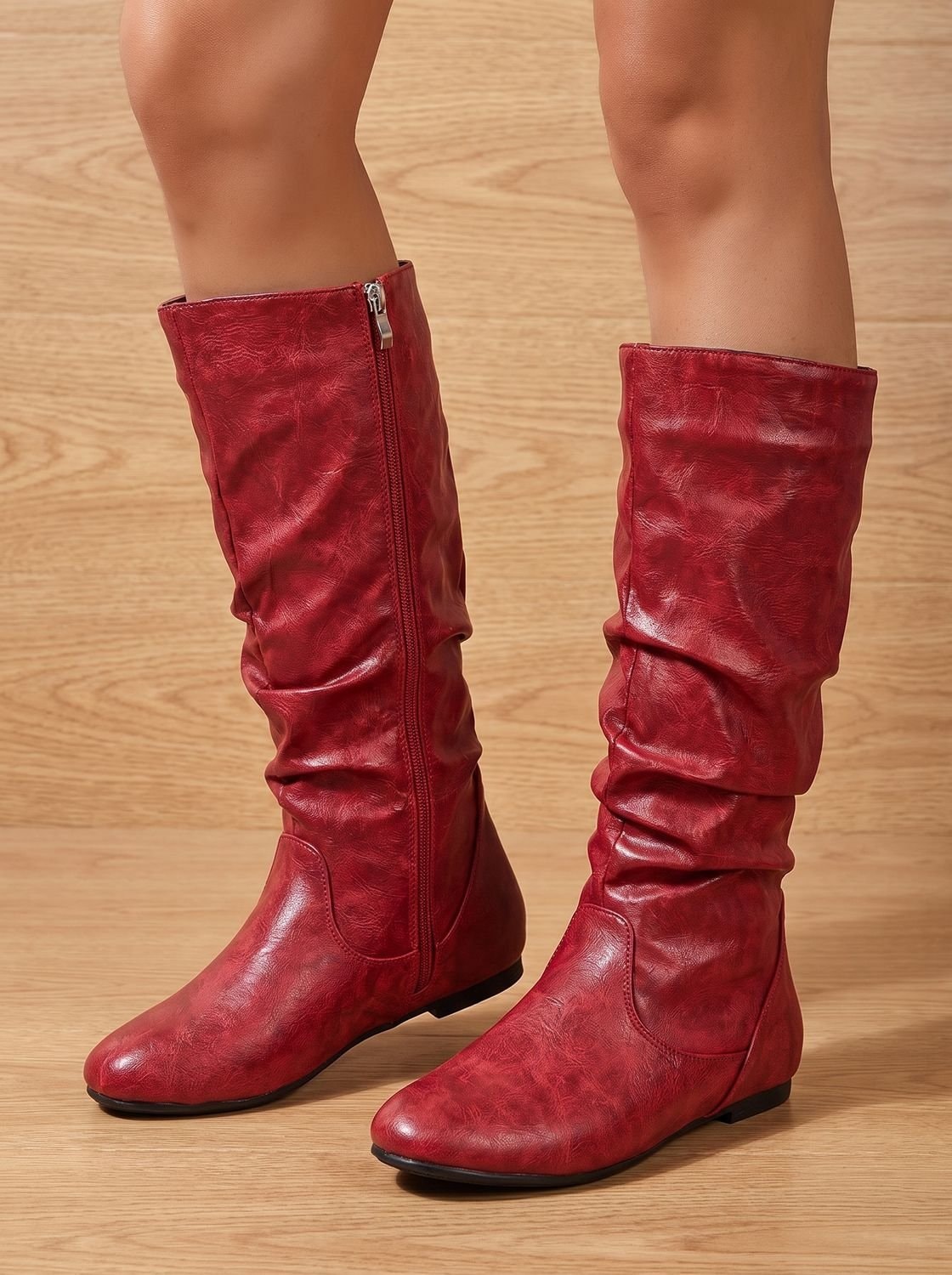 Glossy red knee-high boots standing on a wood floor, viewed from the rear to show both side zippers and ruched shafts.