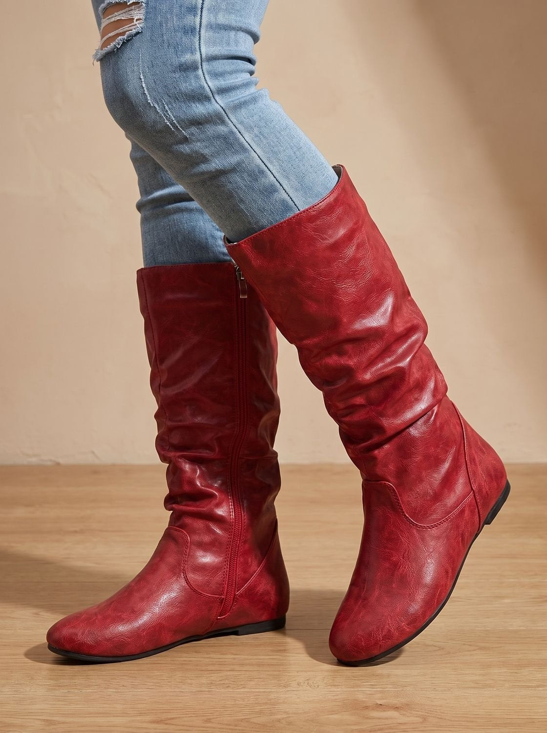 Red knee-high flat boots worn with jeans, shown in a side view that highlights the ruched shaft and rounded toe.