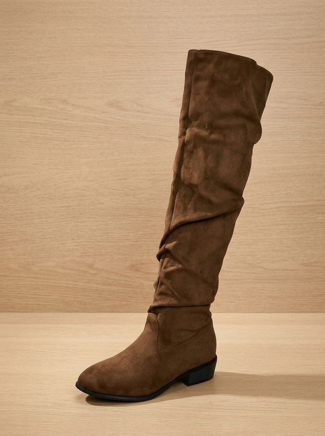 Single brown over-the-knee boot shown in side profile against a wood backdrop.