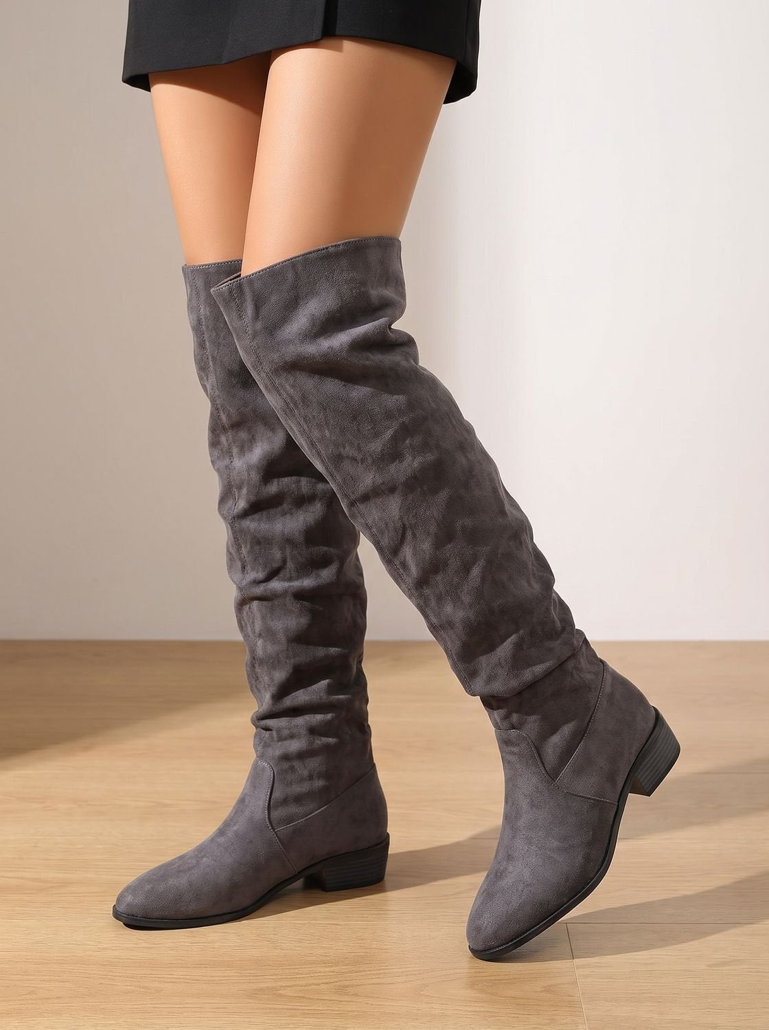 Gray slouchy over-the-knee boots worn with a short dark skirt, showing one raised pointed toe.