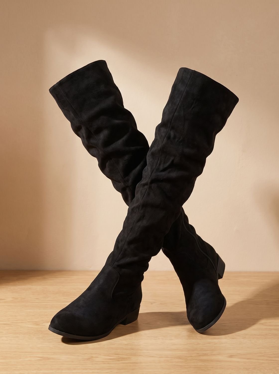Black slouchy over-the-knee boots crossed at the legs, showing their tall ruched shafts and low heels.