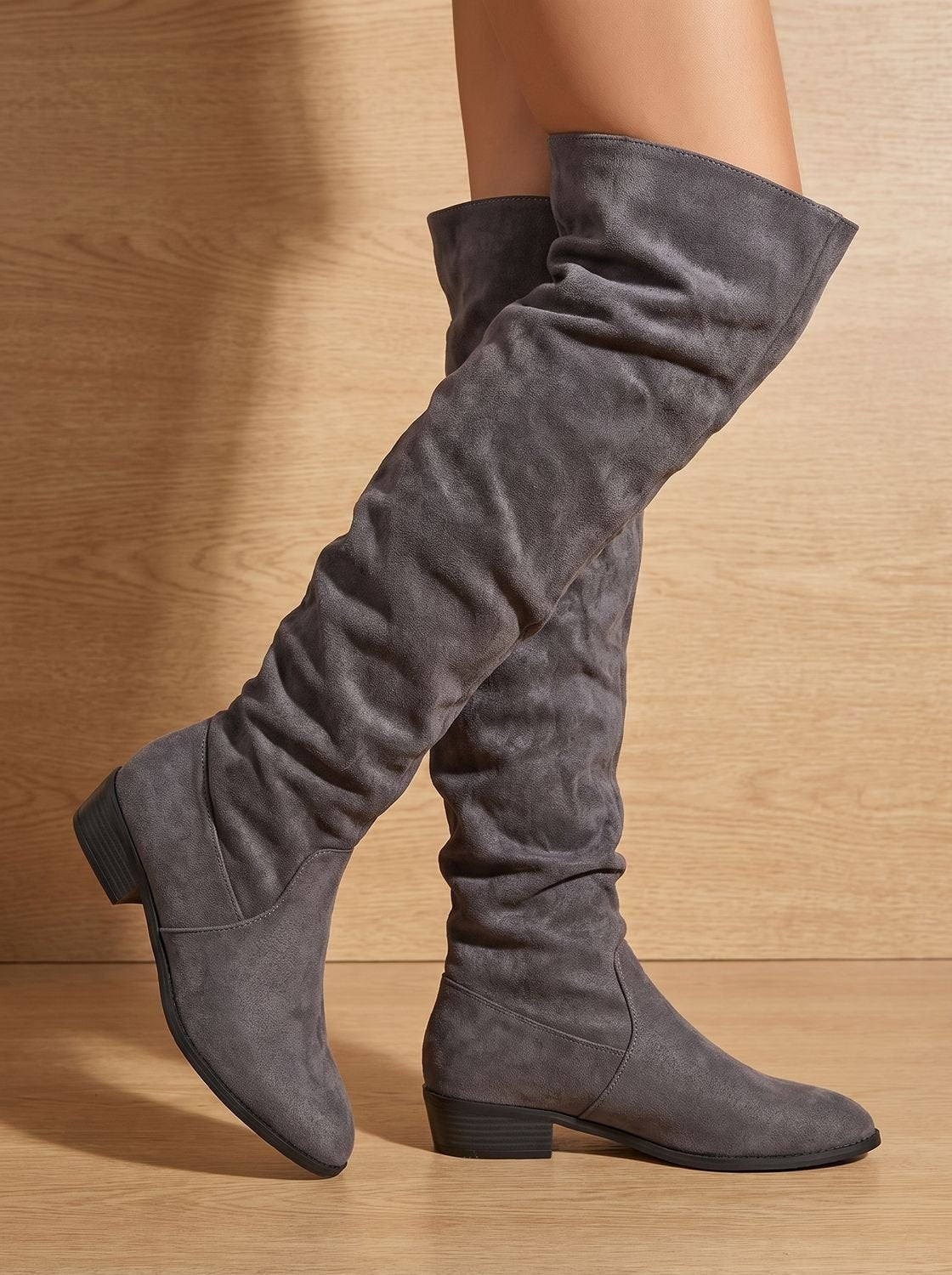 Gray over-the-knee boots in a side view, emphasizing the draped shaft, pointed toe, and low block heel.