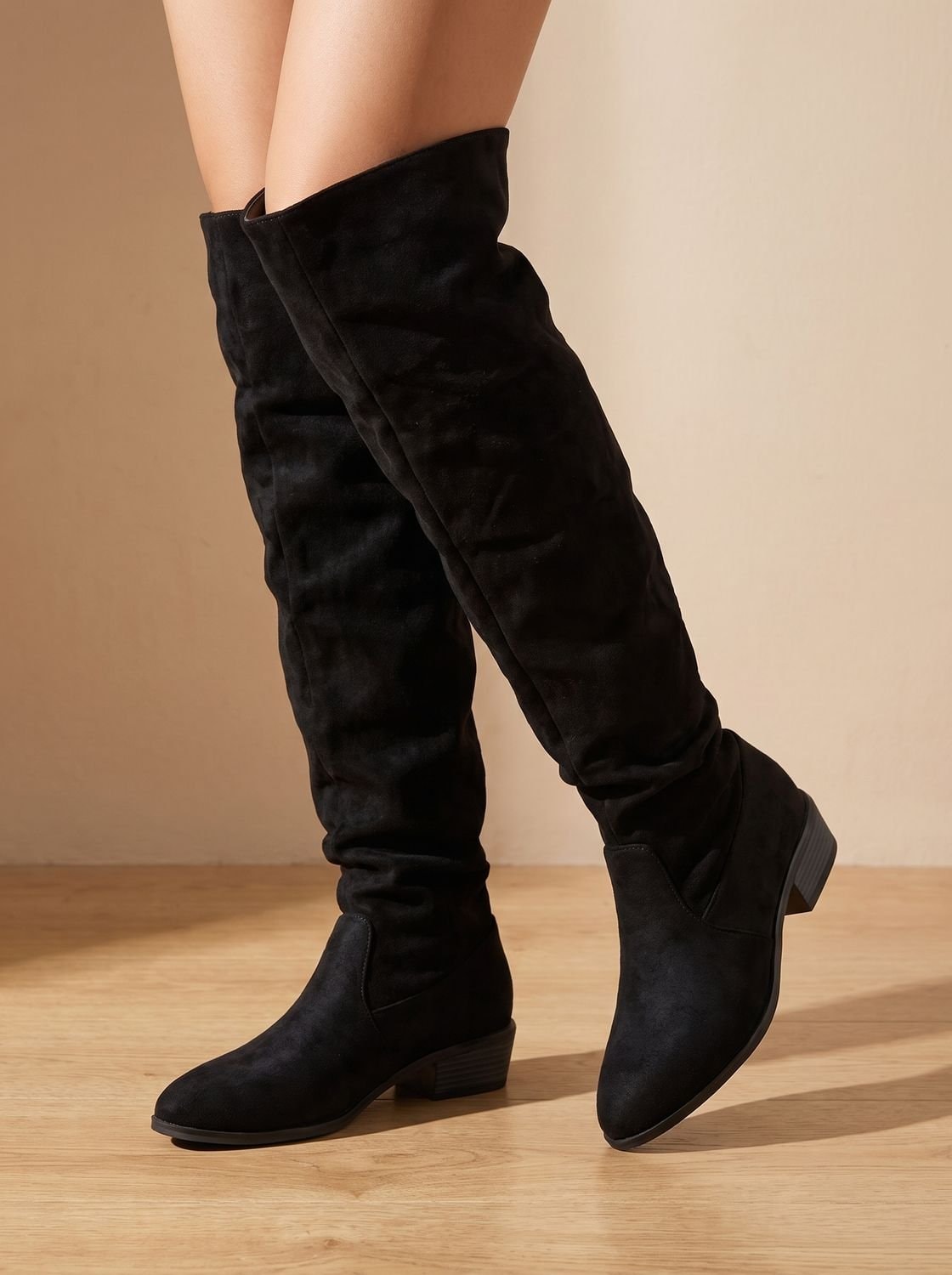 Black over-the-knee boots on a model, showing the relaxed shaft, pointed toe, and low stacked heel.