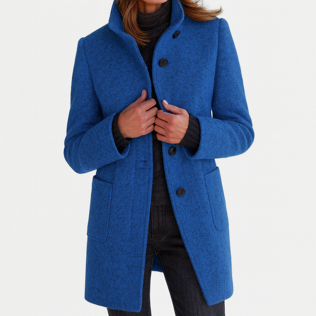 Cobalt blue thigh-length women's coat with a stand collar, button-front closure, long sleeves, and two patch pockets, shown worn over dark layers.