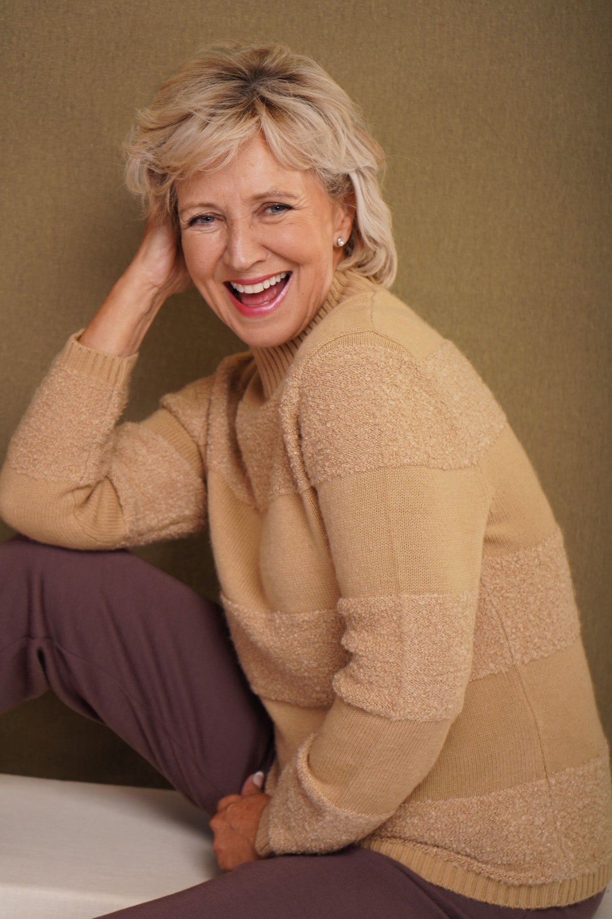 Woman sitting and smiling wearing a relaxed roll neck jumper with horizontal textured looped stripes and ribbed cuffs._0