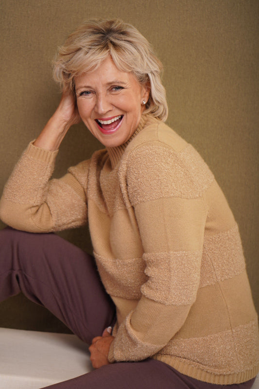 Woman sitting and smiling wearing a relaxed roll neck jumper with horizontal textured looped stripes and ribbed cuffs._0