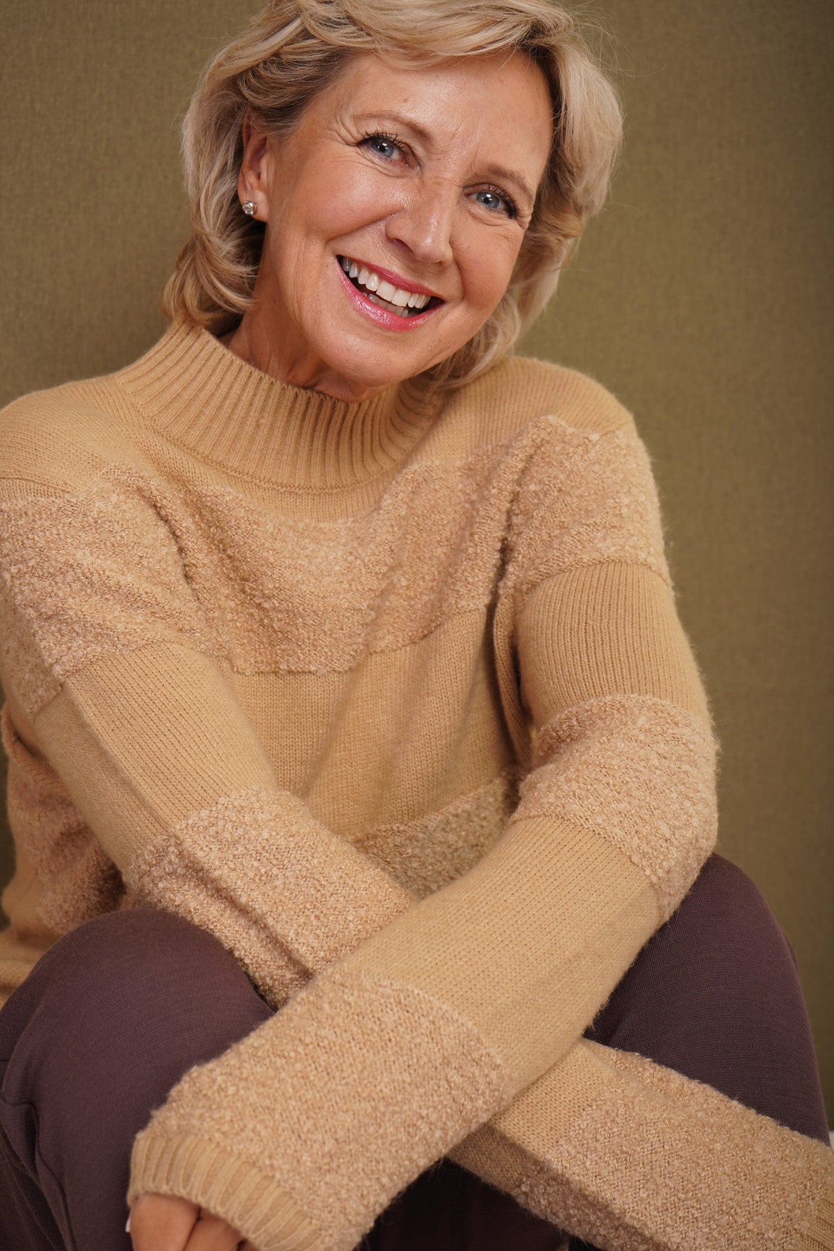 Woman sitting and smiling wearing a relaxed roll neck jumper with horizontal textured looped stripes and ribbed cuffs._1
