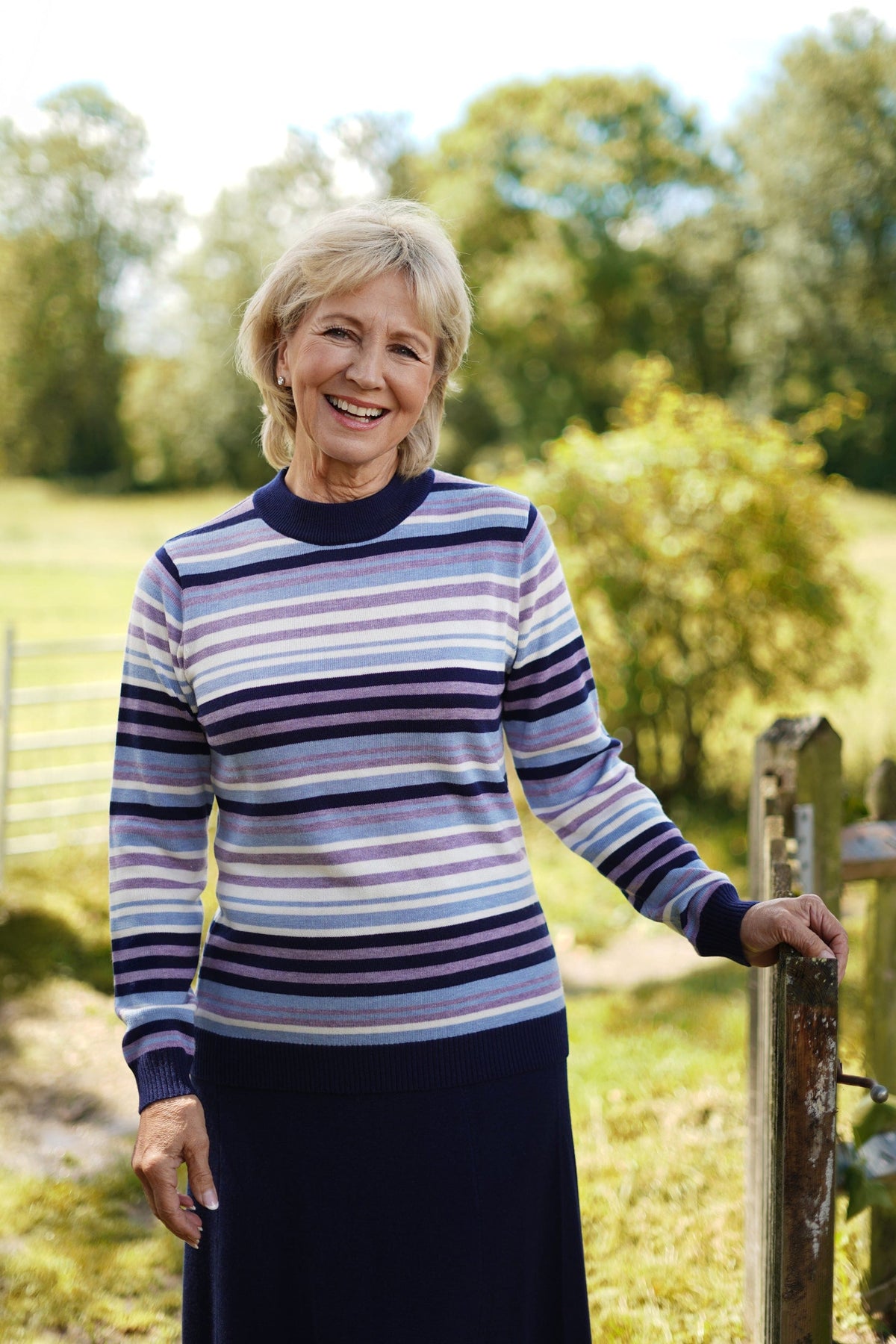 Woman wearing a long sleeve striped knit jumper with a ribbed crew neck, cuffs and hem, standing beside a wooden gate._0