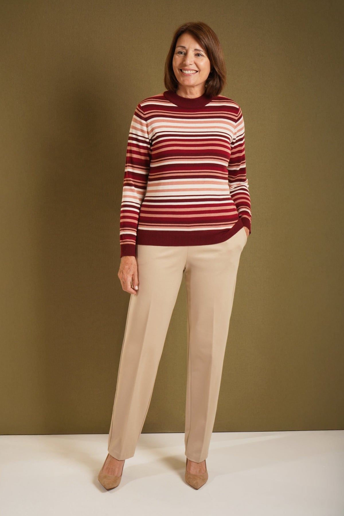 Woman wearing a long sleeve striped knit jumper with a ribbed crew neck, cuffs and hem, standing beside a wooden gate._9