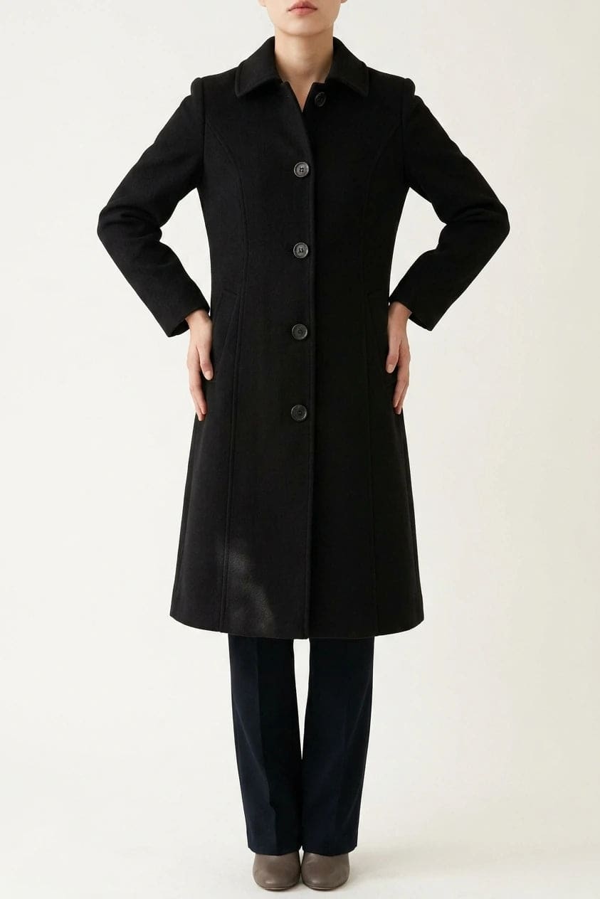 Woman wearing a knee length single breasted coat with a point collar, four front buttons, panel seams and slanted hip pockets, over trousers and ankle boots._0