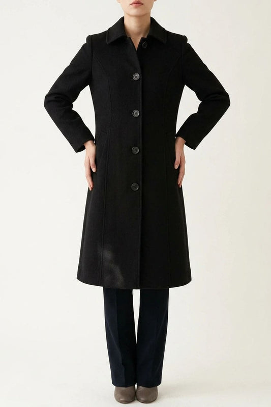 Woman wearing a knee length single breasted coat with a point collar, four front buttons, panel seams and slanted hip pockets, over trousers and ankle boots._0