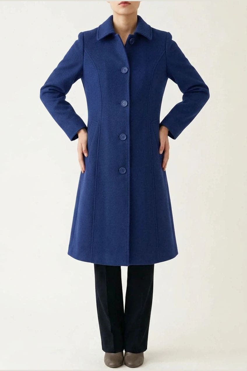 Woman wearing a knee length single breasted coat with a point collar, four front buttons, panel seams and slanted hip pockets, over trousers and ankle boots._1