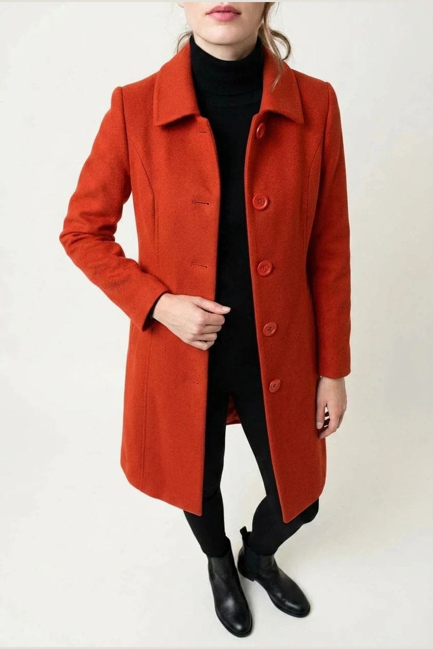 Woman wearing a knee length single breasted coat with a point collar, four front buttons, panel seams and slanted hip pockets, over trousers and ankle boots._11
