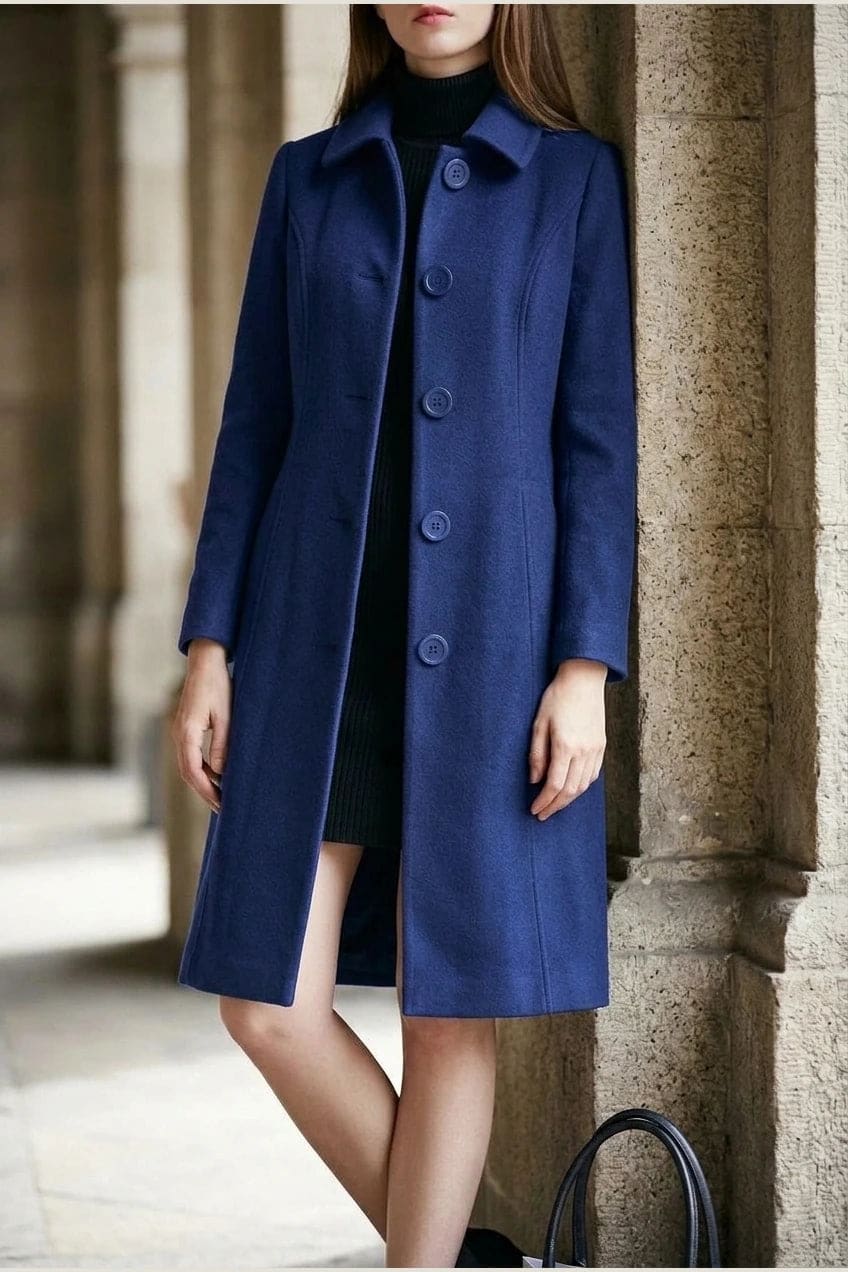 Woman wearing a knee length single breasted coat with a point collar, four front buttons, panel seams and slanted hip pockets, over trousers and ankle boots._2