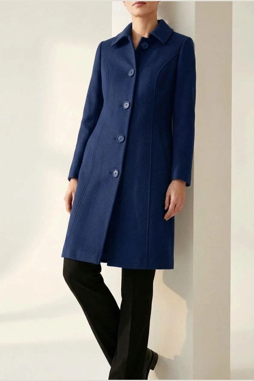 Woman wearing a knee length single breasted coat with a point collar, four front buttons, panel seams and slanted hip pockets, over trousers and ankle boots._3