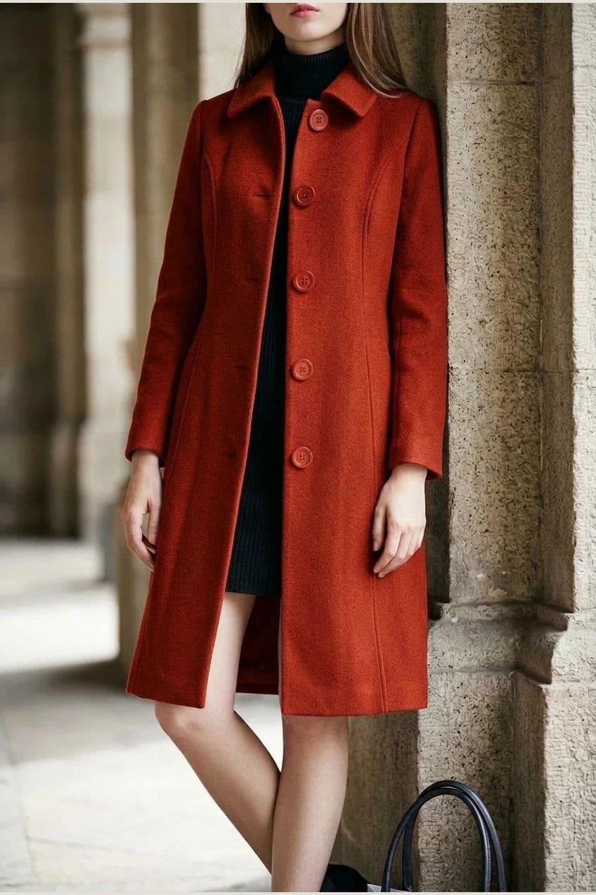 Woman wearing a knee length single breasted coat with a point collar, four front buttons, panel seams and slanted hip pockets, over trousers and ankle boots._8