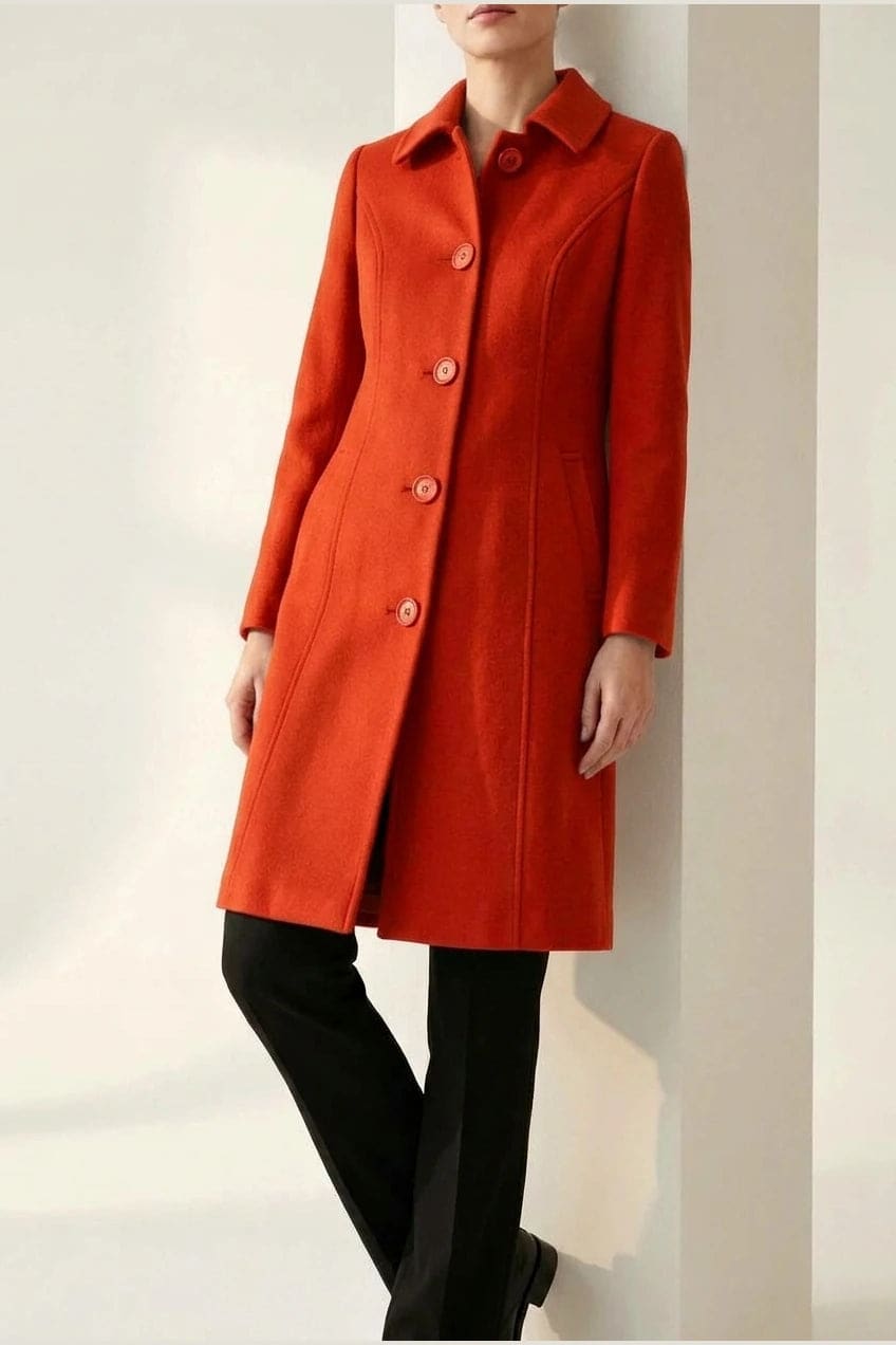 Woman wearing a knee length single breasted coat with a point collar, four front buttons, panel seams and slanted hip pockets, over trousers and ankle boots._9