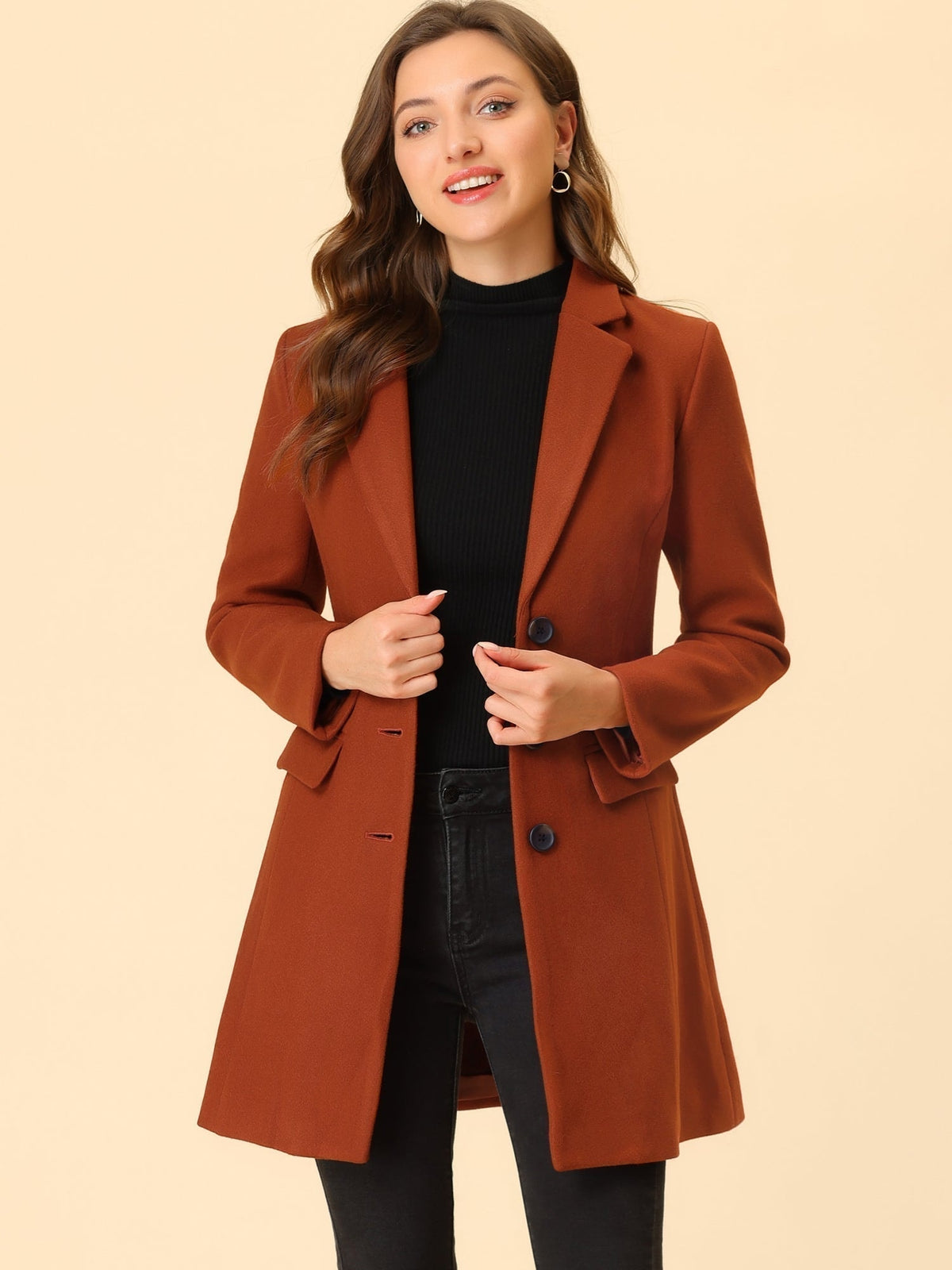 Rust-red tailored coat worn over a black top and jeans, with the model holding both sides of the front.