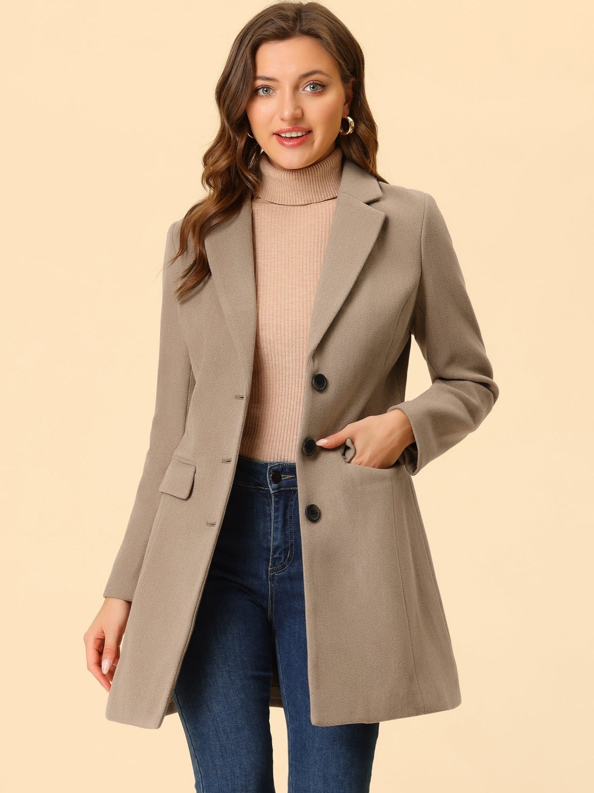 Taupe lapel coat styled over a ribbed turtleneck and blue jeans, with one hand tucked into a flap pocket.