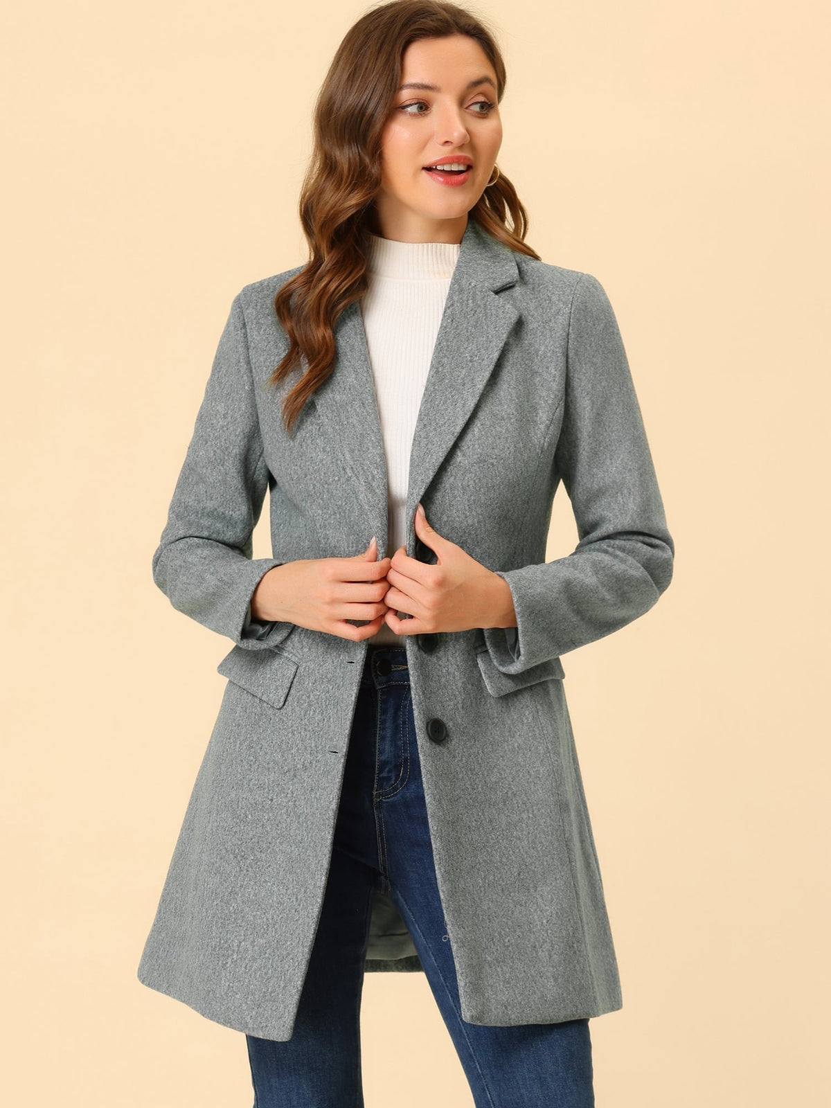 Gray tailored coat worn over a white sweater and jeans, with the model holding the front near the lapels.