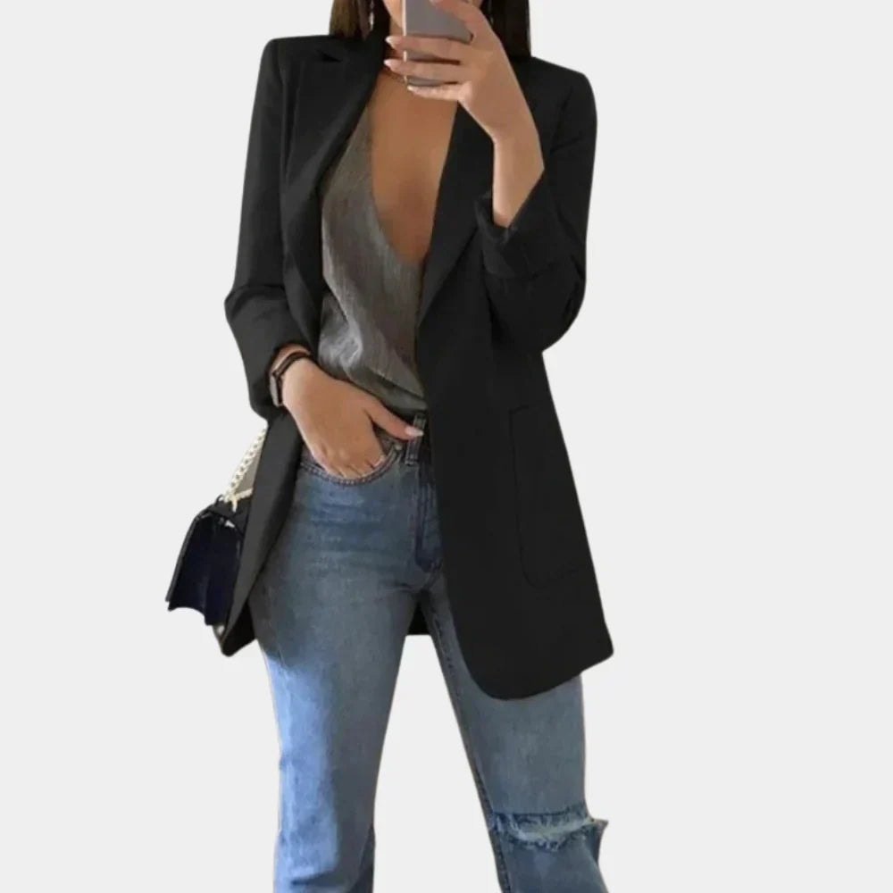 Black tailored longline blazer jacket with notched lapels and front pockets, styled over a gray top and jeans.