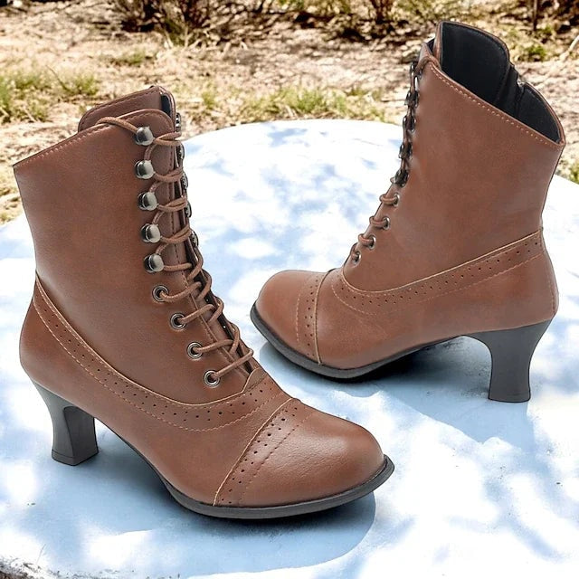 Pair of brown Victorian-inspired lace-up mid-heel boots with perforated detailing, rounded toes, and side zippers.