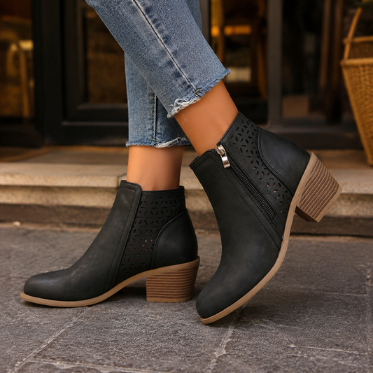 Black cutout ankle boots with rounded toes, side zippers, and mid-height block heels styled with cropped jeans.