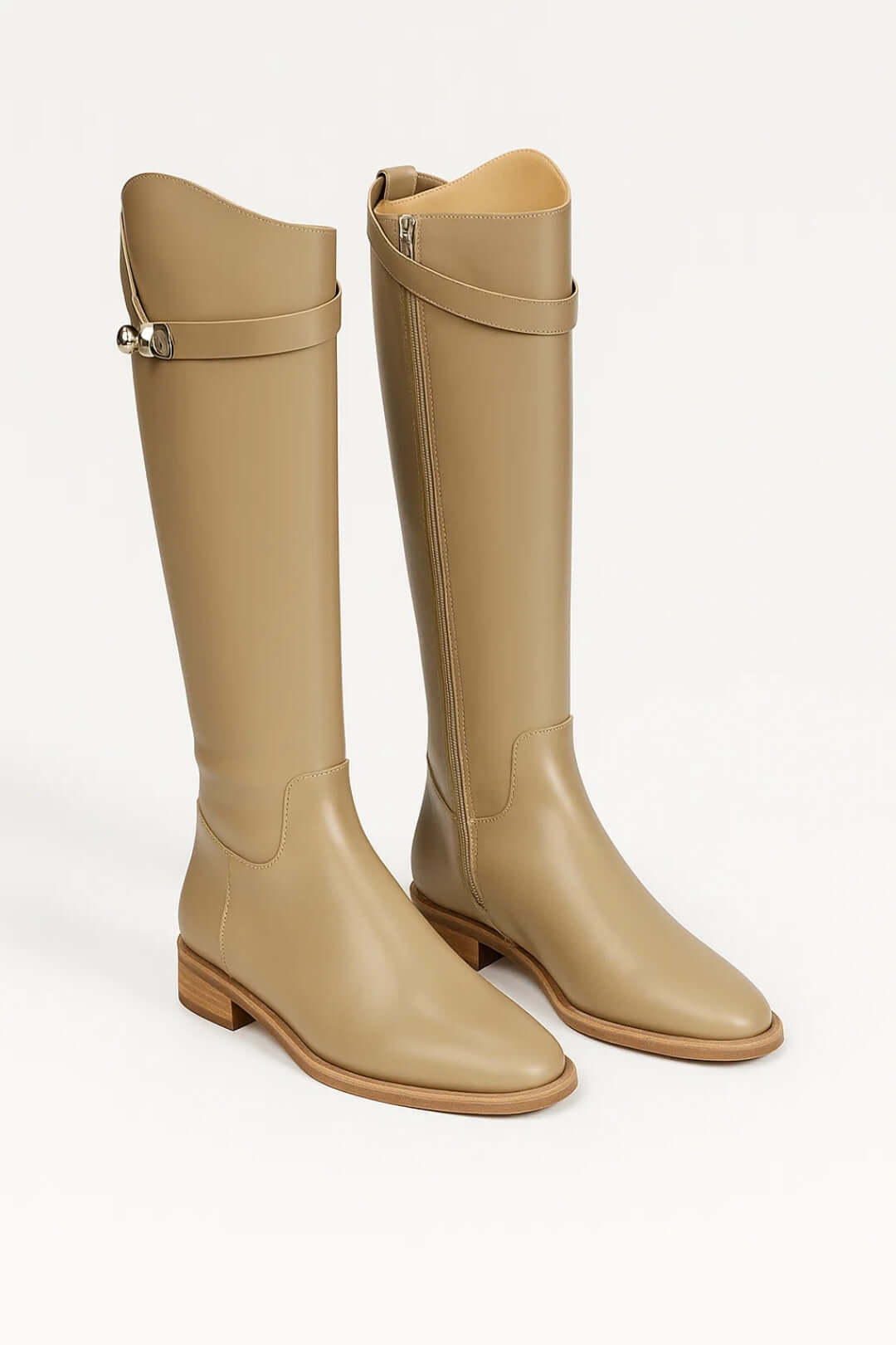 Tan knee-high riding boots with low stacked heels, rounded toes, side seams, and buckle straps around the shafts.
