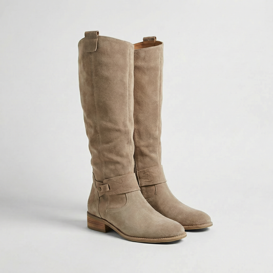 Taupe knee-high slouch boots shown in a three-quarter view with low stacked heels and wraparound buckle straps.