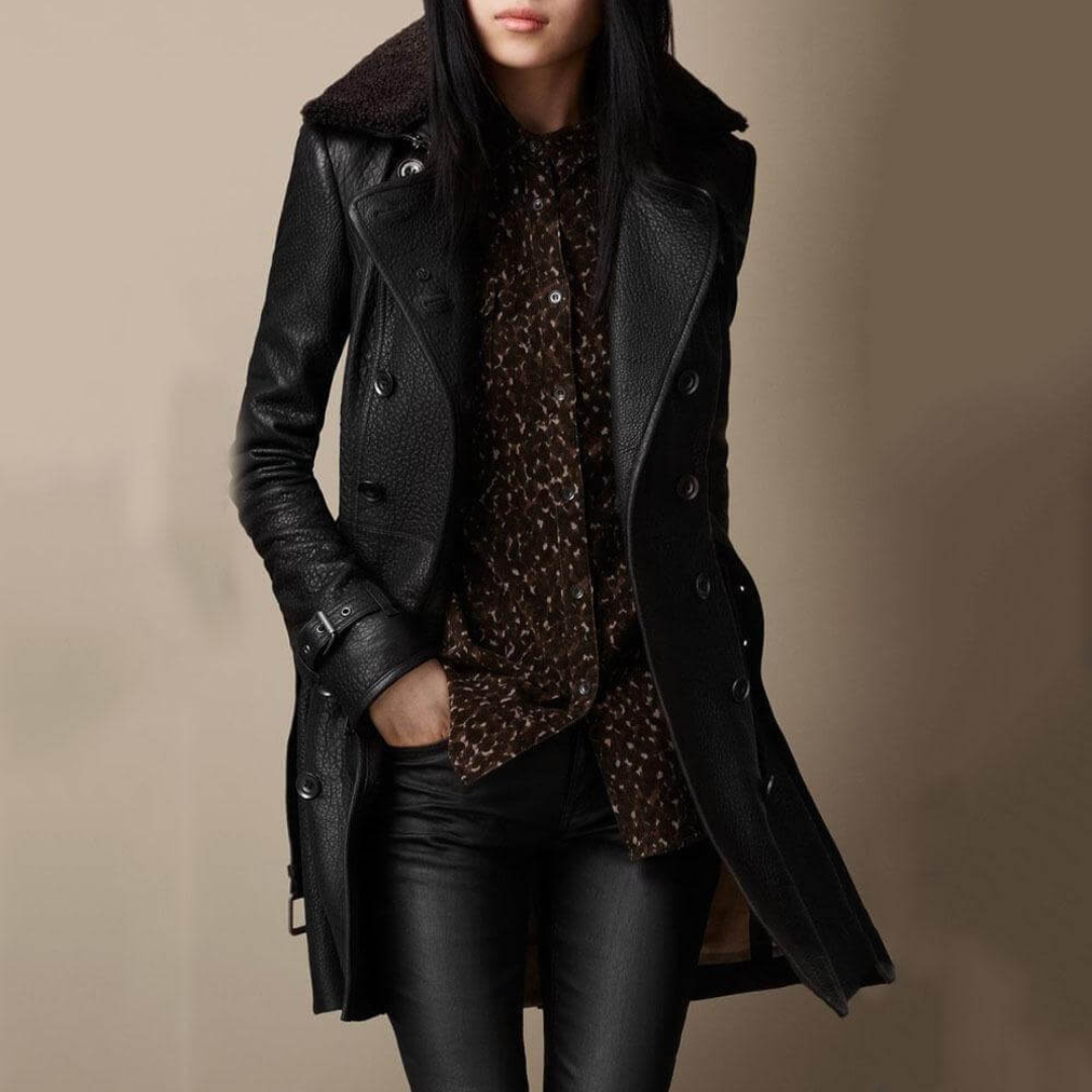 A woman wearing a dark double breasted mid length coat with a wide collar and belted cuffs outdoors._2