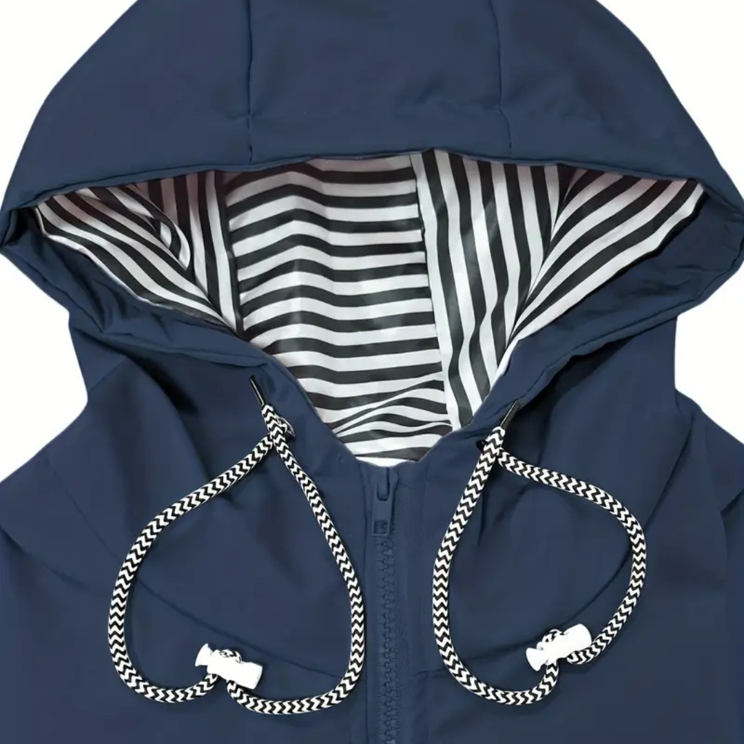 Model wearing a hooded long rain coat with a front zip, drawstring waist, and front pockets on a wet city street._11