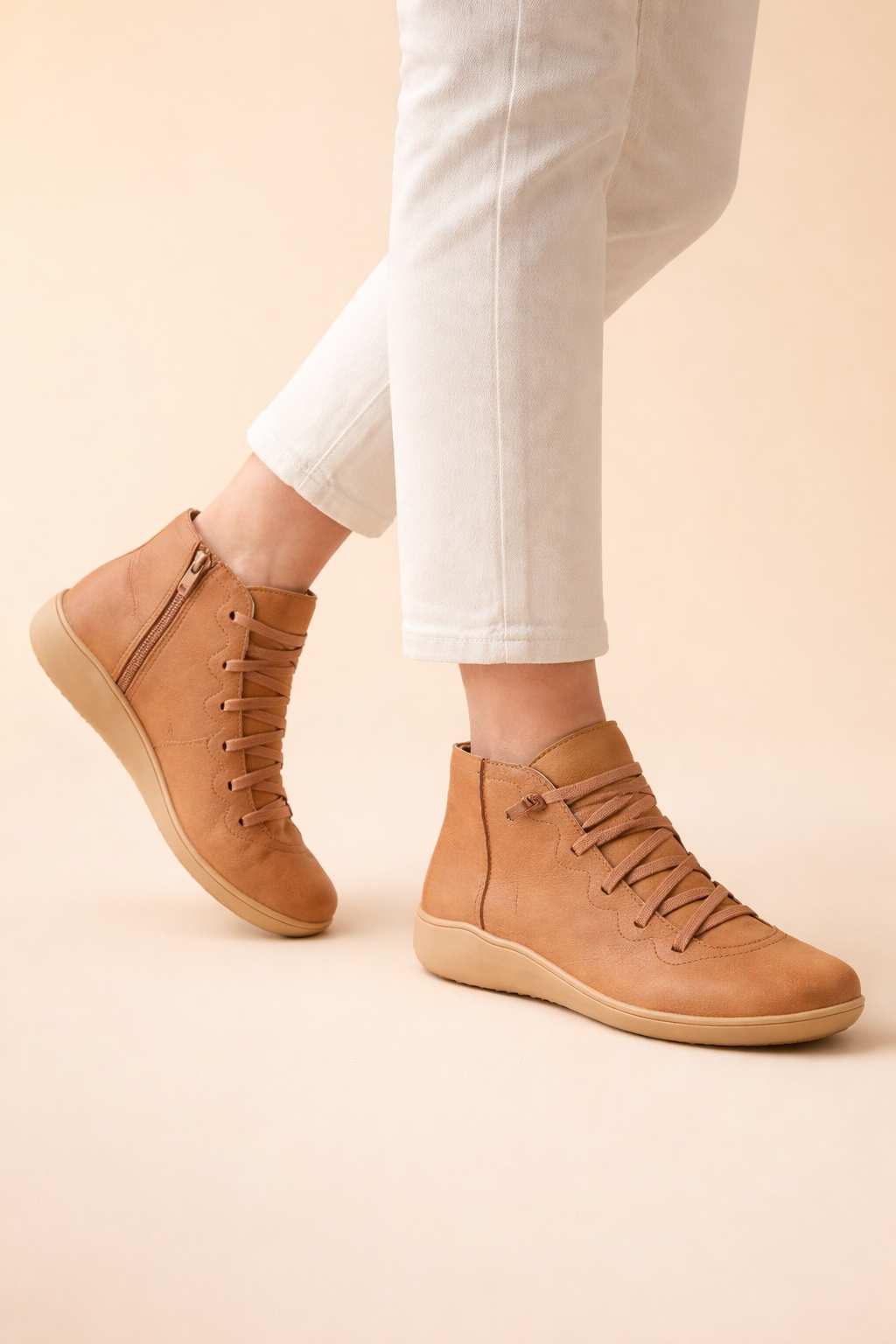 Tan women's lace-up ankle boots with side zips and low-profile soles, styled with white trousers.