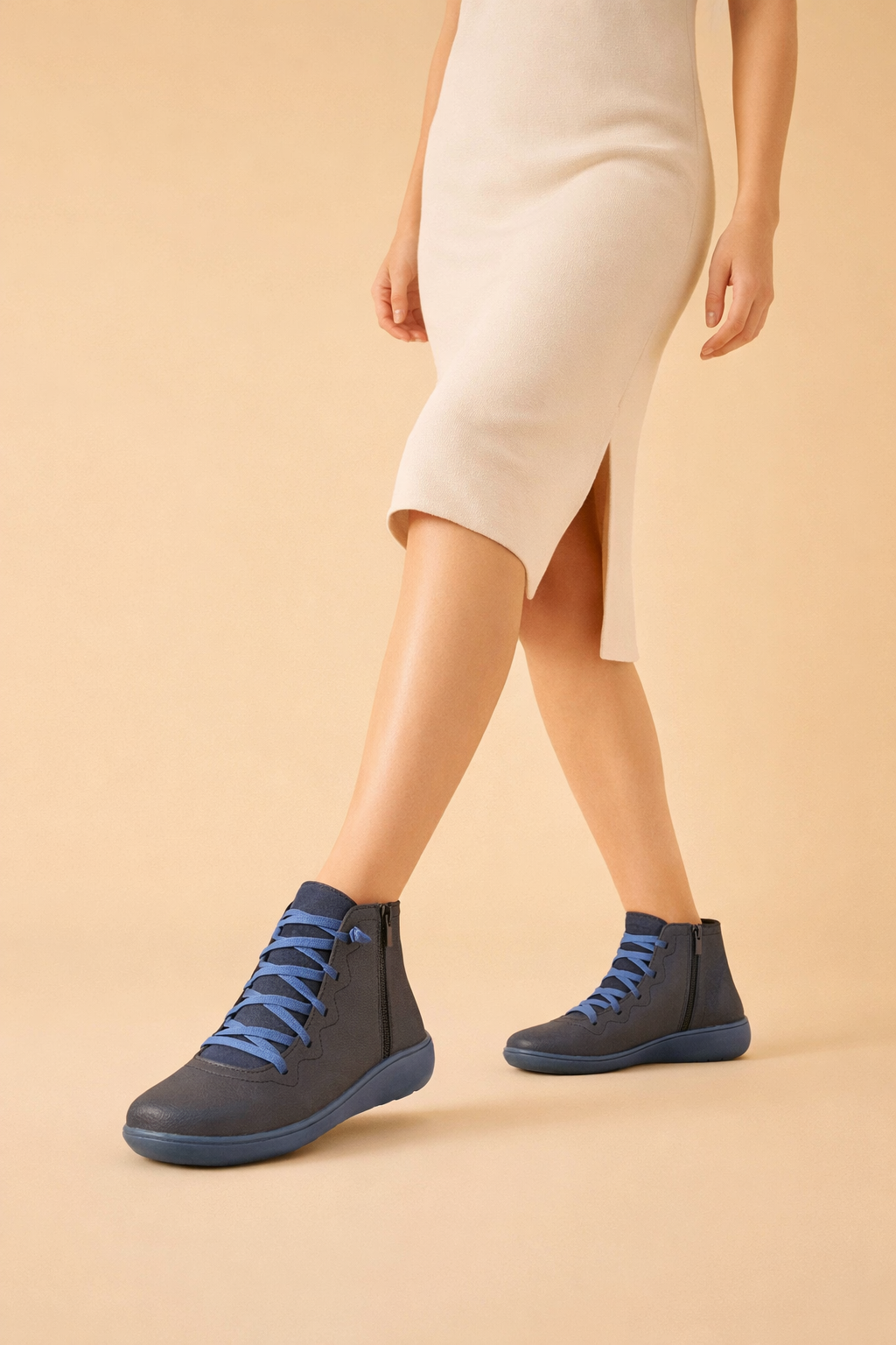 Navy women's lace-up ankle boots with bright blue laces, worn with a cream dress in a walking pose.