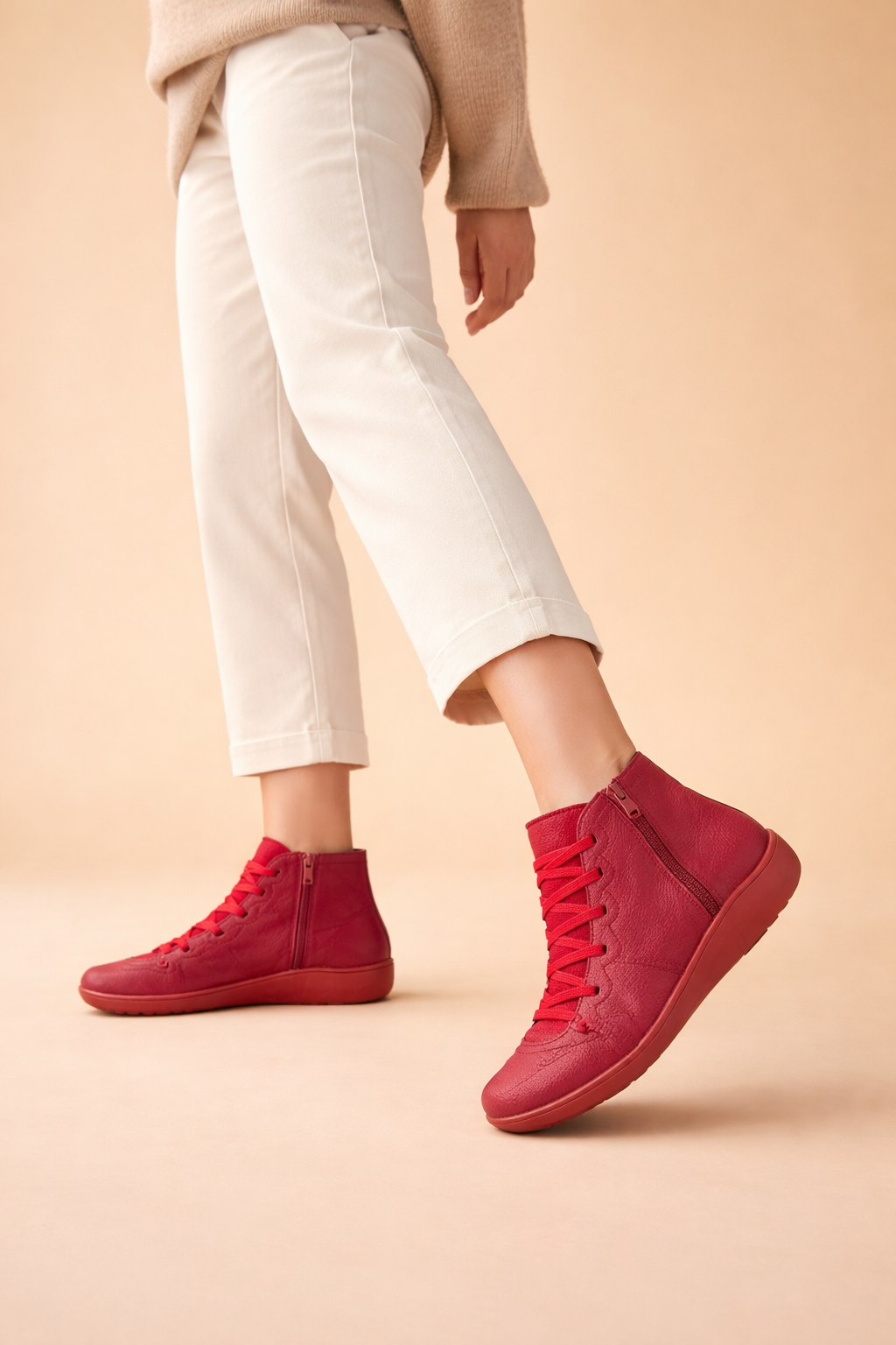 Red women's lace-up ankle boots styled with cropped white trousers, including a raised foot that shows the sole profile.