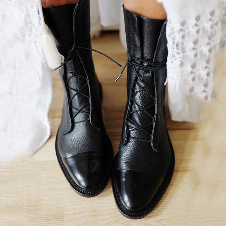 Black mid-calf lace-up boots with glossy rounded toe caps and low block heels, styled with a white lace-trimmed skirt.
