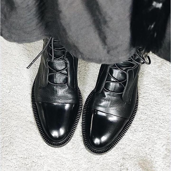 Top-down view of black lace-up boots showing their glossy contrast toe caps, textured uppers, and ridged soles.