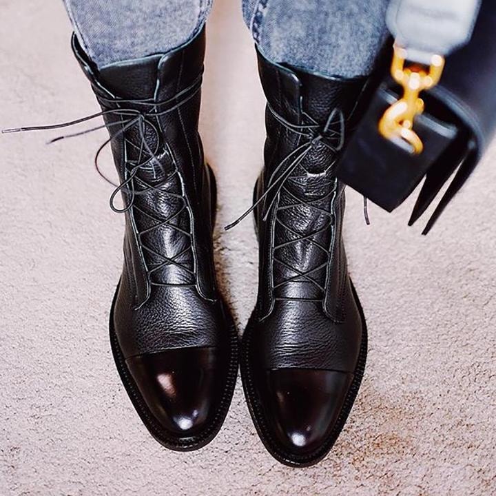 Black mid-calf lace-up boots with contrasting toe caps worn with cuffed jeans and paired with a handbag.