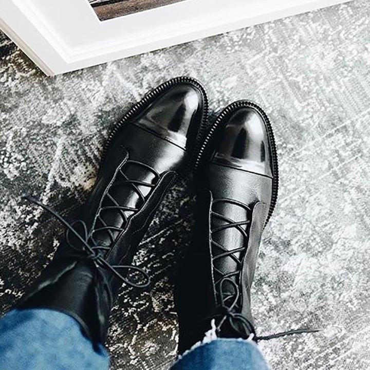 Black lace-up boots viewed from above, showing the crisscross lacing, contrasting toe caps, and low heels with jeans.