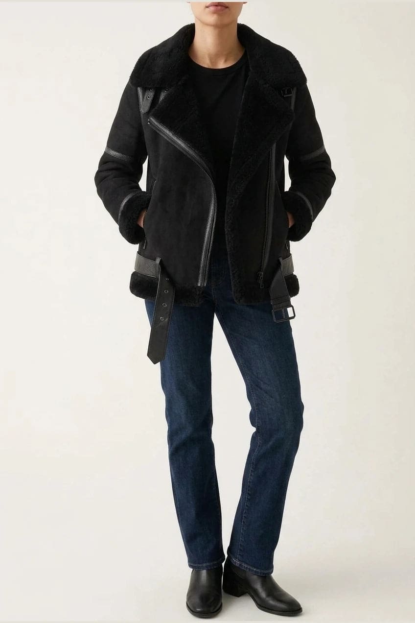 Woman wearing a hip length aviator jacket with a wide fleece collar, asymmetric zip, buckled waist tabs and side pockets, with straight jeans and ankle boots._1